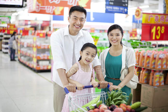 Chinesische Familie posiert mit Einkaufswagen im Supermarkt — Stockfoto