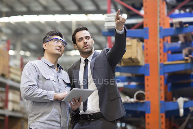 Бізнесмен та інженер, використовуючи цифровий планшет та розмовляючи на заводі — стокове фото