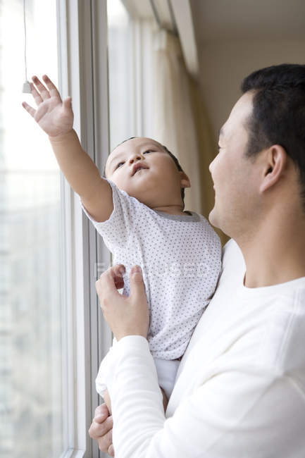 Chinois homme avec bébé garçon debout par la fenêtre — Photo de stock