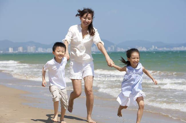 Chinese mother with kids running on sunny beach — Stock Photo
