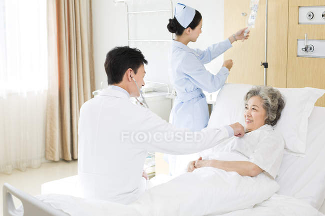 Médico chino usando estetoscopio en paciente en hospital - foto de stock