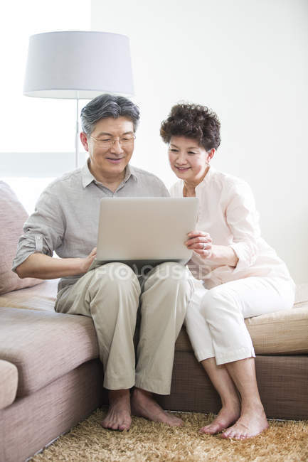 Chinois couple aîné en utilisant ordinateur portable ensemble sur le canapé — Photo de stock