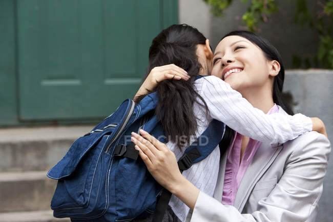 Mujer china y colegiala abrazándose en la calle - foto de stock