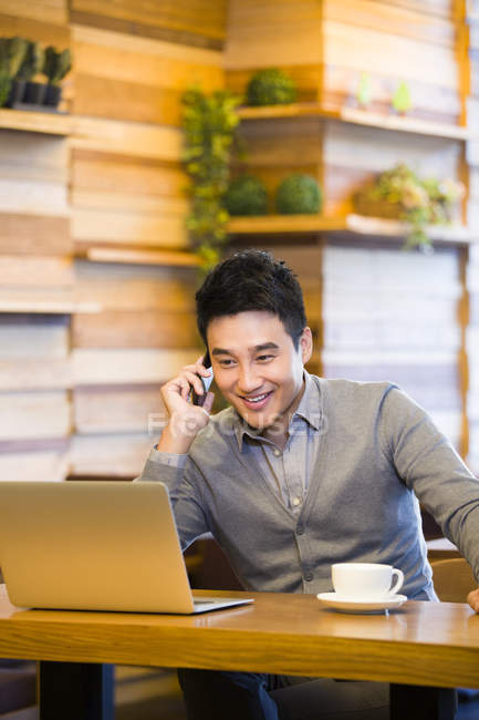 Chinese telefoniert und schaut in Café auf Laptop — Stockfoto