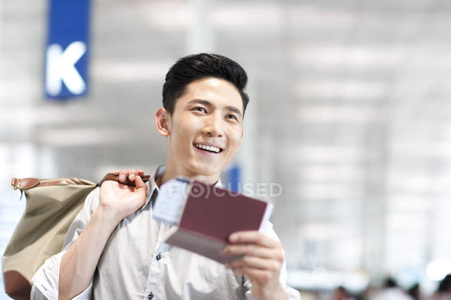 Excited chinese man at airport with ticket and passport — Stock Photo