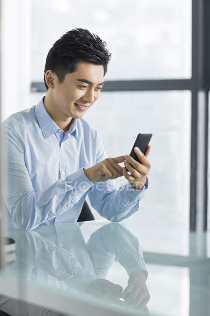 Китайский бизнесмен за столом в офисе использует смартфон — стоковое фото
