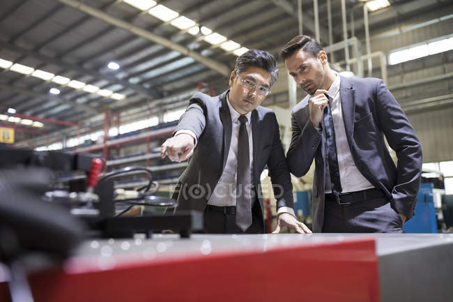 Des hommes d'affaires examinent des machines dans une usine industrielle — Photo de stock