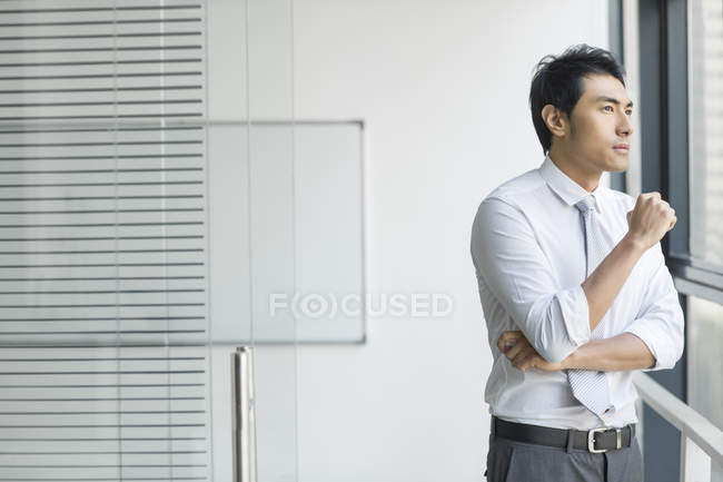 Hombre de negocios chino mirando por la ventana en la oficina - foto de stock
