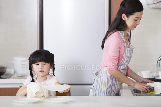 Madre e hija chinas lavando y secando platos - foto de stock