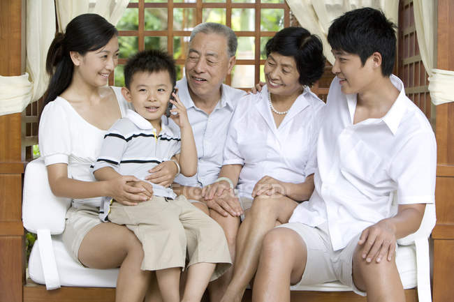 Китайская семья сидит на скамейке, пока мальчик разговаривает по телефону — стоковое фото