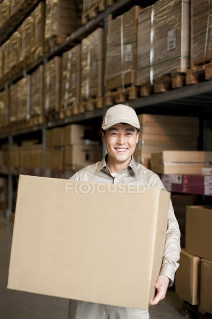 Masculino chinês armazém trabalhador transportando caixa de papelão — Fotografia de Stock