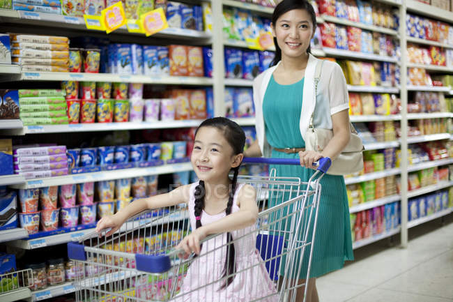 Chinese mother pushing daughter in shopping cart in supermarket — Stock Photo