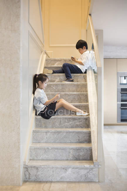 Китайський хлопчик і дівчинка використання смартфонів на сходах — стокове фото