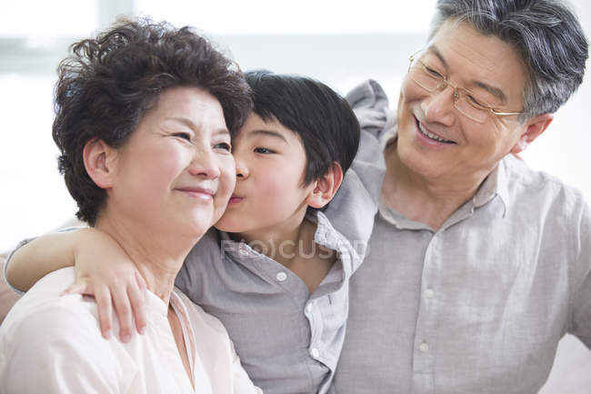 Chinese grandson embracing grandparents and kissing grandmother — Stock Photo