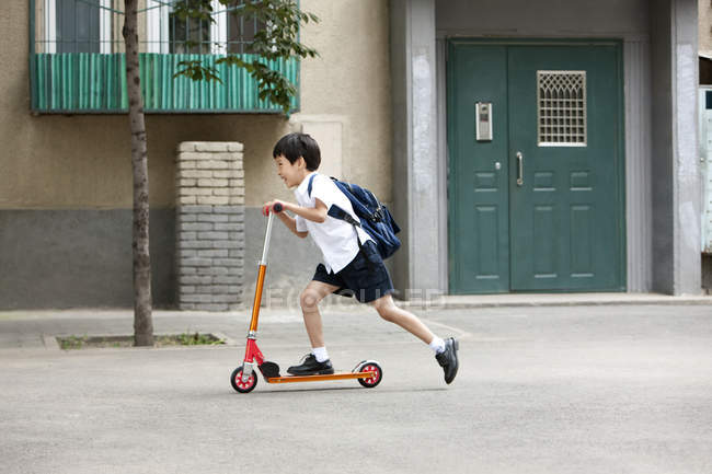 Chino niño a caballo empuje scooter en la calle - foto de stock