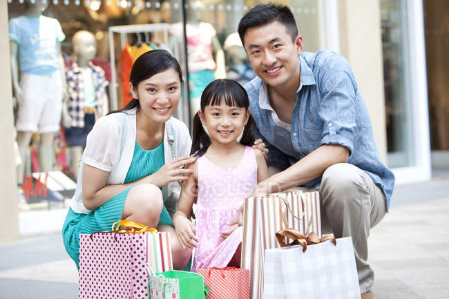Pais chineses e filha posando com sacos de compras no shopping — Fotografia de Stock