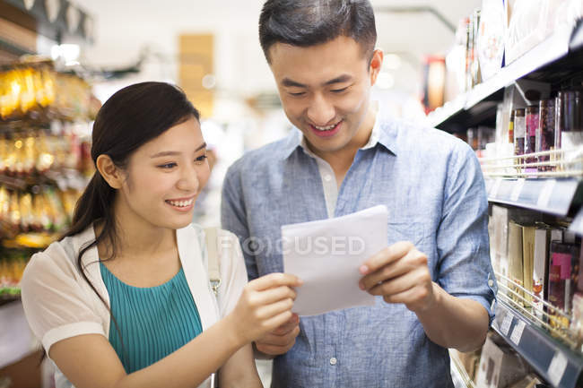 Coppia cinese leggere la lista della spesa nel supermercato — Foto stock
