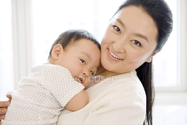 Donna cinese che tiene il bambino sul petto e sorride — Foto stock