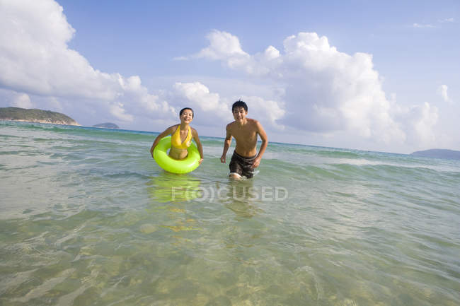 Jovem casal andando com anel inflável na água do mar — Fotografia de Stock
