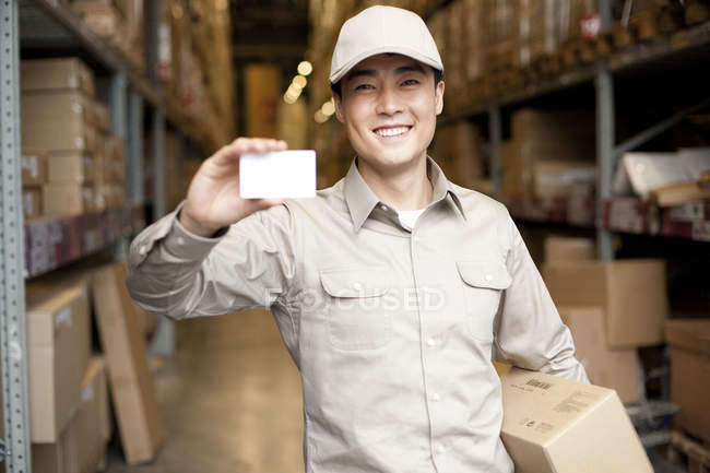 Male Chinese warehouse worker holding blank business card — Stock Photo