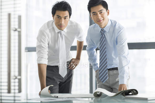 Chinese businessmen standing at desk with blueprint in office — Stock Photo