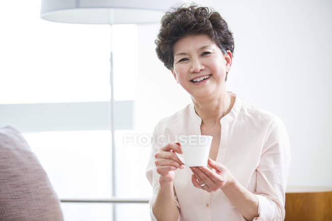 Mulher chinesa sorrindo com xícara de café nas mãos — Fotografia de Stock