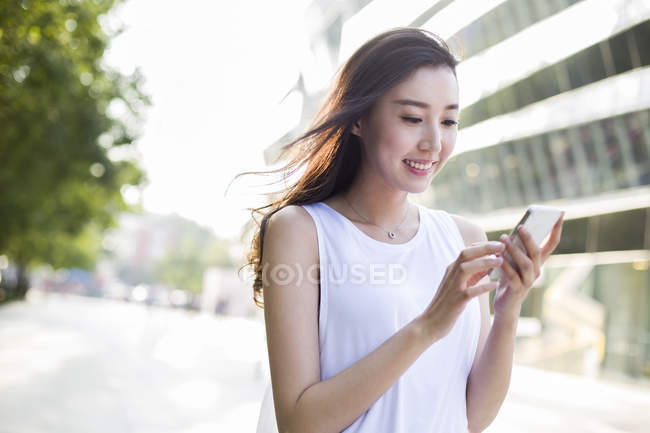 Mujer china mirando hacia abajo en el smartphone en la calle - foto de stock