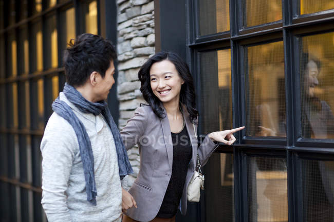 Femme chinoise pointant vers la fenêtre du magasin tout en se promenant avec l'homme — Photo de stock