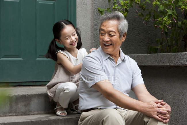 Китайская внучка массирует дедушку на крыльце — стоковое фото