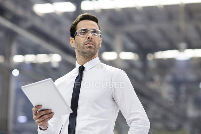 Бизнесмен в защитных очках держит цифровой планшет на заводе — стоковое фото