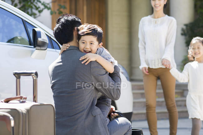 Filho chinês cumprimentando e abraçando pai retornando na rua — Fotografia de Stock