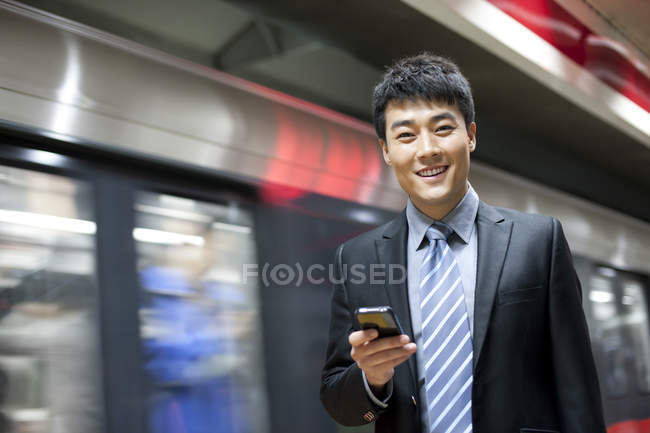 Homme d'affaires chinois utilisant un smartphone à la station de métro — Photo de stock