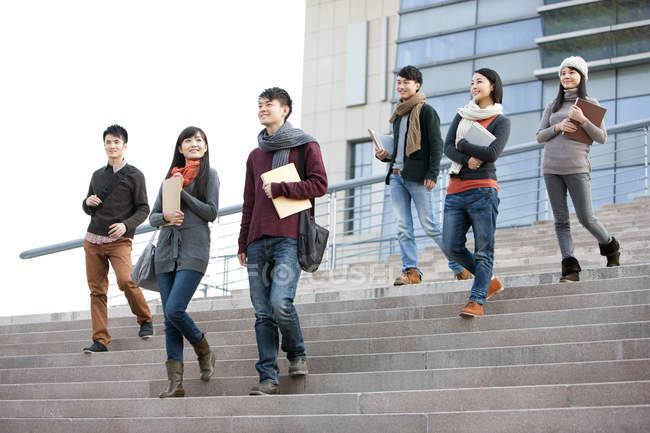 Estudiantes universitarios chinos caminando por los escalones del edificio universitario - foto de stock
