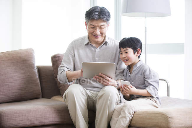 Abuelo y nieto chino usando tableta digital en sofá - foto de stock