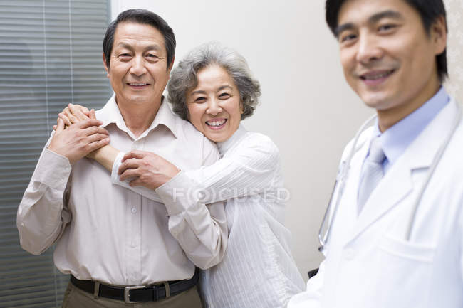 Chinese doctor with hugging senior couple in hospital — Stock Photo