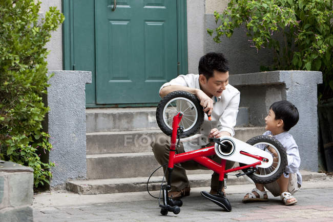 Китайский отец и сын чинят велосипед на крыльце — стоковое фото
