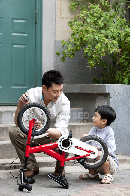 Chinese father and son fixing bicycle on porch — Stock Photo