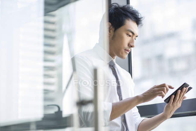 Китайський бізнесмен за допомогою смартфона в дверях в офісі — стокове фото