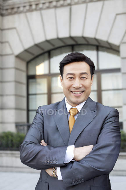 Retrato del empresario chino con los brazos cruzados en la ciudad - foto de stock