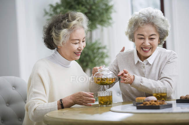 Senior mujeres chinas sonriendo y vertiendo té - foto de stock