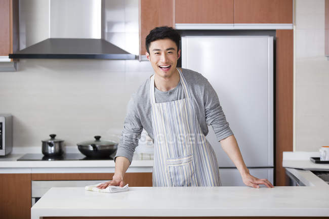 Chinese young man cleaning kitchen with rag and looking in camera — Stock Photo