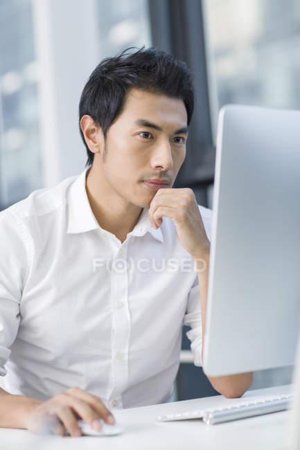 Pensativo empresario chino utilizando la computadora en la oficina - foto de stock