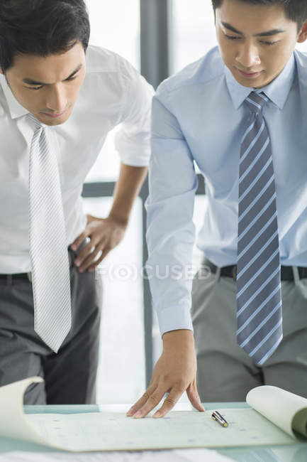 Chinese businessmen discussing blueprint at desk in office — Stock Photo