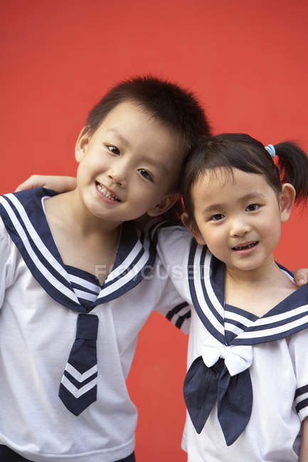 Chinese elementary students embracing on red background — Stock Photo