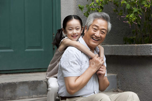 Abuelo y nieta chinos abrazándose en el porche - foto de stock