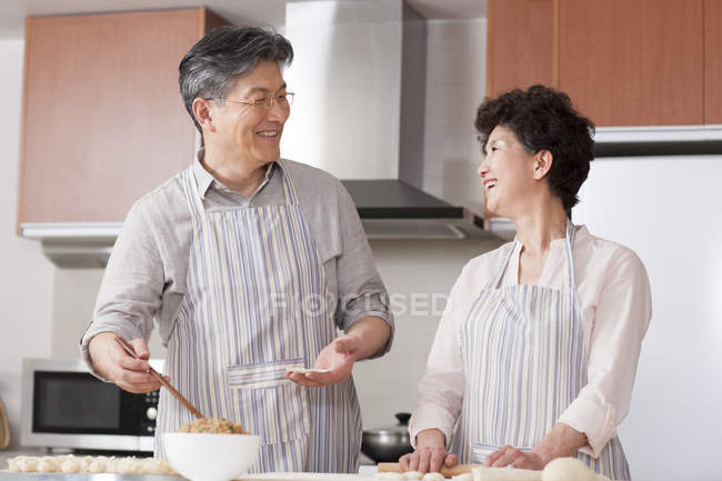 Senior Chinese couple making dumplings together in kitchen — Stock Photo