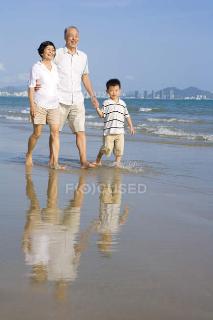 Китайские бабушка с дедушкой и внуком прогуливаются по пляжу — стоковое фото