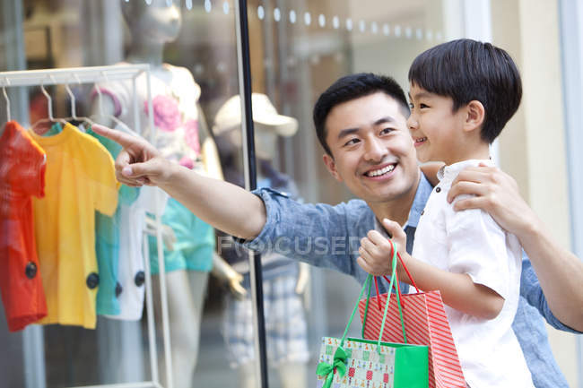 Padre e figlio cinese che puntano alla finestra del negozio con le borse della spesa — Foto stock