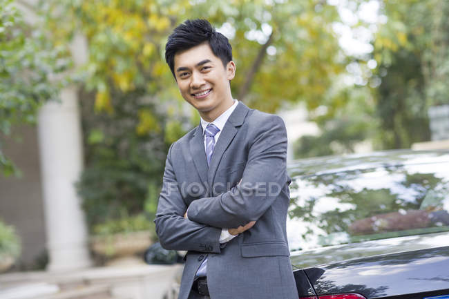 Portrait of Chinese businessman leaning on car on street — Stock Photo