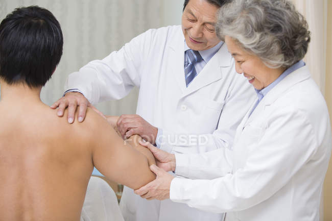 Старшие китайские врачи делают массаж пациенту мужского пола — стоковое фото